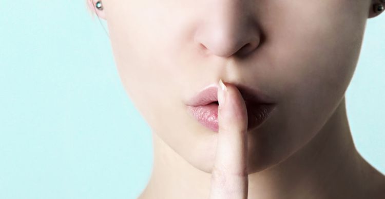 A picture of a woman, with part of her face showing, putting a single finger on her lips as if telling you to keep quiet